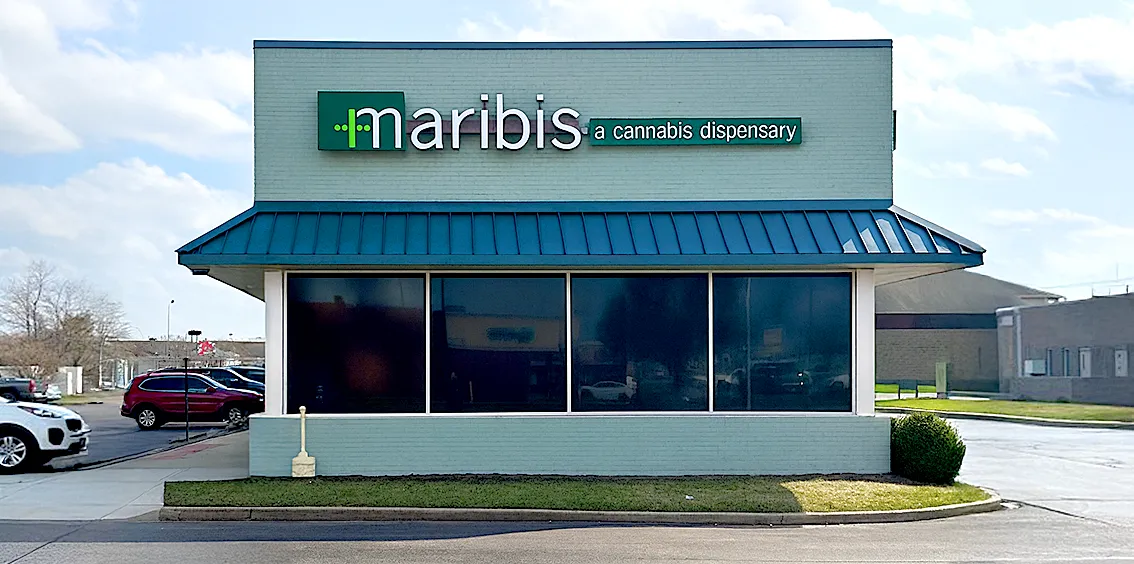 Exterior of Maribis of Springfield cannabis dispensary at 2451 Denver Drive in Springfield, Illinois, showing the teal brick building with blue metal awning, large front windows, parking area, and Maribis “a cannabis dispensary” signage.